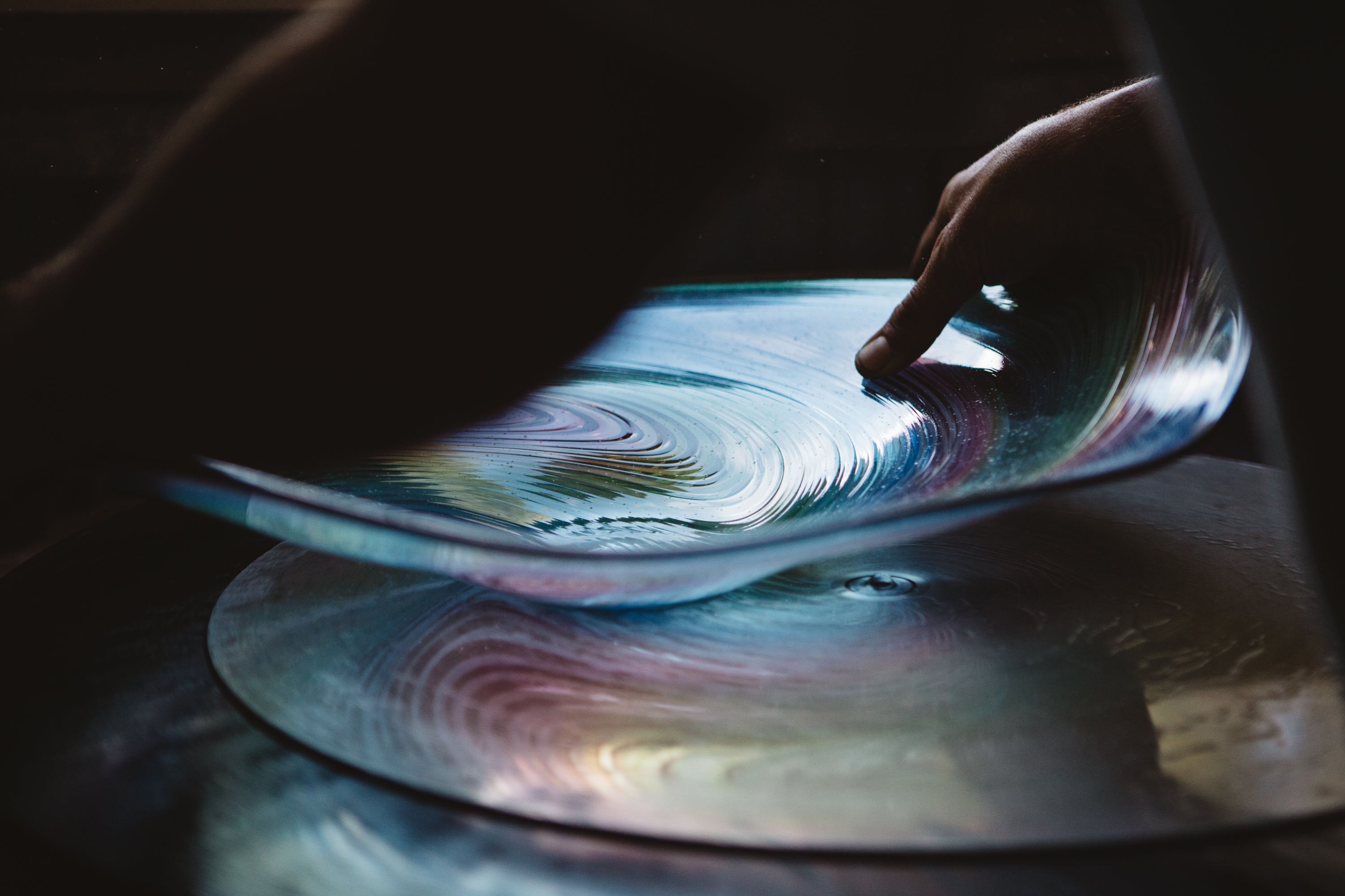 Hand touching a hand blown glass surface with colourful reflections of New Zealand artist Justin Jason